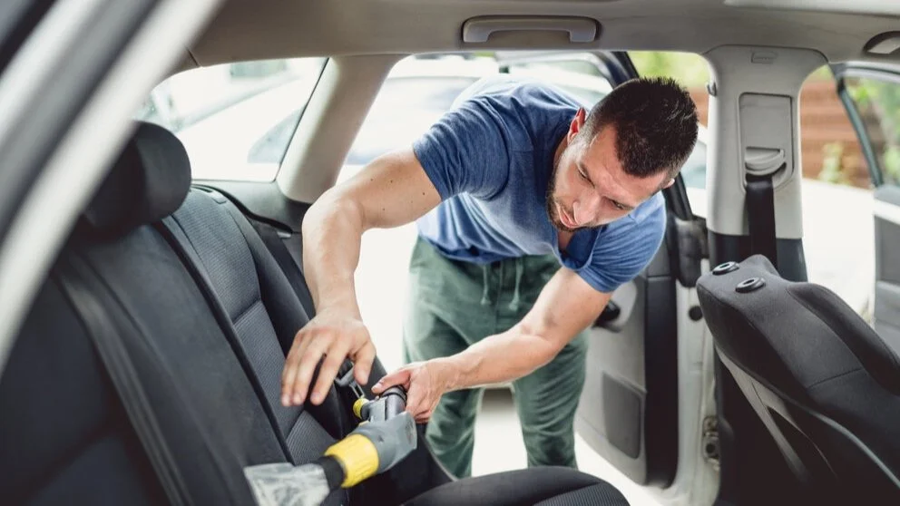 Technician extracting dirt from a fabric rear seat with an upholstery tool