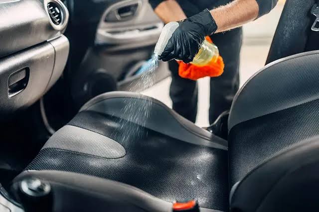 Gloved technician spraying cleaner onto a black car seat